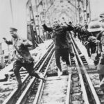 Soviet Red Army prisoners of war captured during Operation Barbarossa, the Nazi German invasion of Russia are forced to cross a railway bridge with no footwear and their arms raised in surrender on the Romanian front in Ukraine circa August 1941. During the Second World War over 3 million Soviet prisoners of war would die in Nazi captivity through starvation, execution, malnutrition and disease. (Photo by Keystone/Hulton Archive/Getty Images).